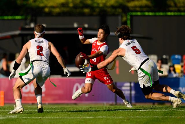 Canada's Emile Chenevert (R) and Japan's Kodai Okumura (C) fight for the ball during the men's match between Japan and Canada at the "IFAF World Flag" World Championship in flag football in Duesseldorf, western Germany, on August 14, 2026. (Photo by Ina FASSBENDER / AFP)