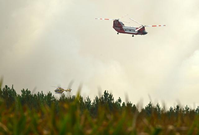 An Australian New South Wales Rural Fire Service (RFS) CH-47D Chinook water-bombing helicopter and a Civil Security helicopter fly above the forest of Luglon during a wildfire, south-western France on August 14, 2026. (Photo by Gaizka IROZ / AFP)