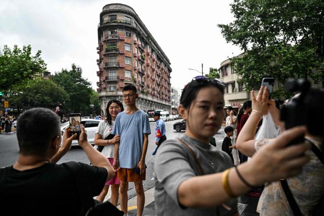 People pose for pictures in front of the Wukang Mansion, a protected historic building, in the Xuhui district in Shanghai on August 14, 2026. (Photo by Hector RETAMAL / AFP)
