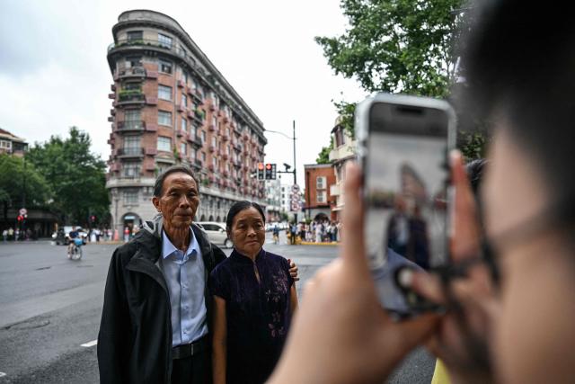 A couple pose for pictures in front of the Wukang Mansion, a protected historic building, in the Xuhui district in Shanghai on August 14, 2026. (Photo by Hector RETAMAL / AFP)