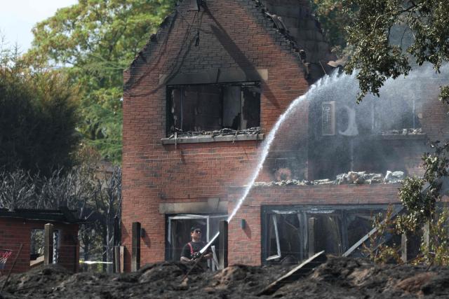 A firefighter puts water onto the smoldering garden of a fire-damaged house, south of Stourbridge town centre in central England on August 14, 2026. Firefighters continued Friday to extinguish wildfires that began on August 13, tearing through several homes, with residents evacuated and "extensive" damage reported. (Photo by Darren Staples / AFP)