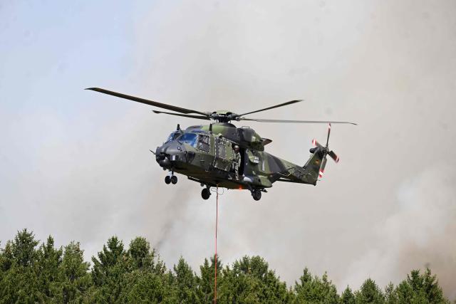 A German armed helicopters loads water to fight a forest fire in Huertgenwald, western Germany Friday, August 14, 2026. Around 1,800 people had to leave their homes in western Germany overnight as a wildfire spread nearby, officials said, with helicopters and army equipment deployed to help battle the flames. A district of the town of Huertgenwald near the Belgian and Dutch borders was evacuated after the fire expanded from 25 hectares (around 60 acres) to 300 hectares by Friday morning. (Photo by Roberto Pfeil / AFP)