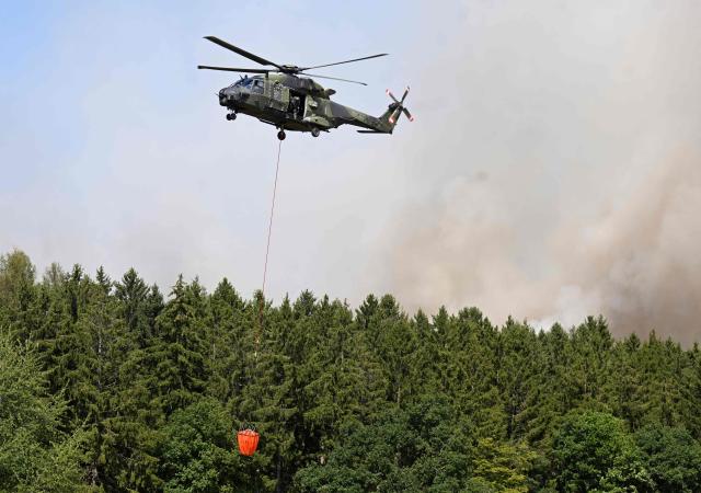 A German armed helicopters loads water to fight a forest fire in Huertgenwald, western Germany Friday, August 14, 2026. Around 1,800 people had to leave their homes in western Germany overnight as a wildfire spread nearby, officials said, with helicopters and army equipment deployed to help battle the flames. A district of the town of Huertgenwald near the Belgian and Dutch borders was evacuated after the fire expanded from 25 hectares (around 60 acres) to 300 hectares by Friday morning. (Photo by Roberto Pfeil / AFP)
