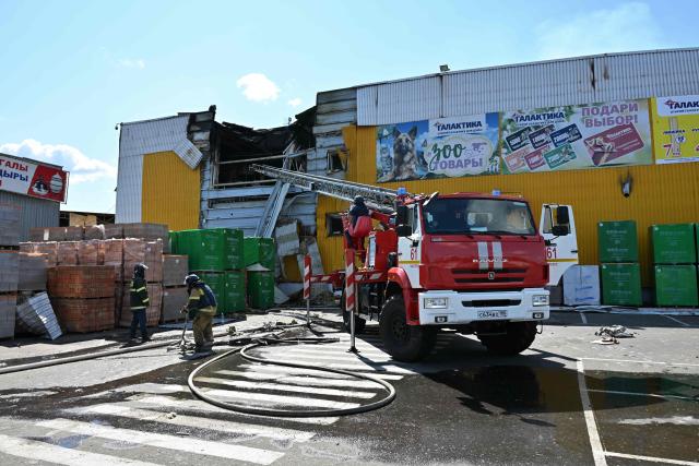 Firefighters work on the grounds of a burned DIY and construction materials mall following an overnight attack, which local Russian-installed officials called Ukrainian drone strikes, in Yenakiyeve in the Donetsk region, Russian-controlled Ukraine, on August 14, 2026, amid the ongoing Russian-Ukrainian conflict. (Photo by AFP)