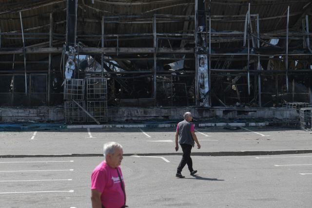 Men walk on the grounds of a burned DIY and construction materials mall following an overnight attack, which local Russian-installed officials called Ukrainian drone strikes, in Yenakiyeve in the Donetsk region, Russian-controlled Ukraine, on August 14, 2026, amid the ongoing Russian-Ukrainian conflict. (Photo by AFP)