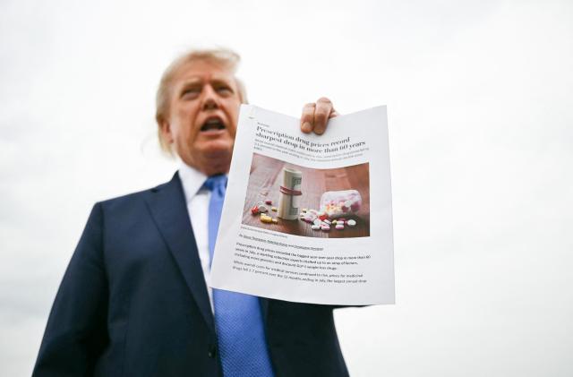 US President Donald Trump shows a press article about drug prices drops as he speaks to the press before boarding  Air Force One at Joint Base Andrews, Maryland, on August 14, 2026. Trump is on his way to Garden City, New York, to speak at the Nassau County Police Academy Center for Training and Intelligence before continuing to Bedminster, New Jersey, to spend the weekend at his golf club. (Photo by Kent NISHIMURA / AFP)