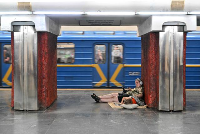 A woman adjusts the blanket covering her sleeping son as they take shelter in a metro station in anticipation of a Russian missile strike that night, in Kyiv on August 14, 2026, amid the Russian invasion of Ukraine. (Photo by Sergei SUPINSKY / AFP)