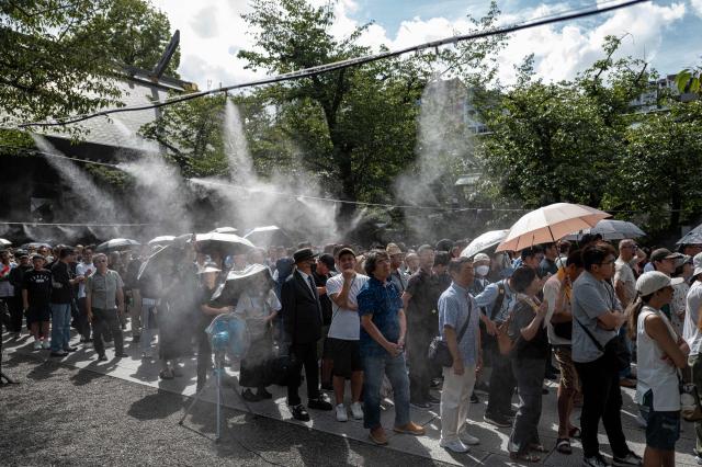 People queue up near water misters to pay their respect during a visit to the Yasukuni Shrine in Tokyo on August 15, 2026, on the 81st anniversary of Japan's surrender in World War II. Yasukuni is dedicated to 2.5 million war dead, mostly Japanese, including convicted war criminals involved in Imperial Japan's invasion and occupation of parts of Asia in the 1930s and 1940s. (Photo by Philip FONG / AFP)