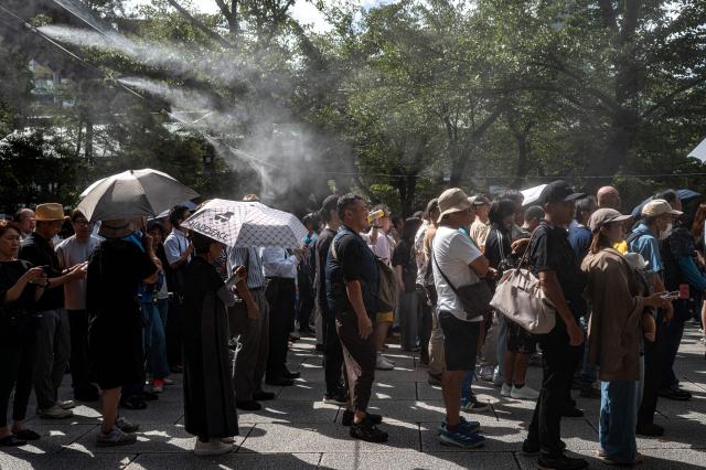 People queue up near water misters to pay their respect during a visit to the Yasukuni Shrine in Tokyo on August 15, 2026, on the 81st anniversary of Japan's surrender in World War II. Yasukuni is dedicated to 2.5 million war dead, mostly Japanese, including convicted war criminals involved in Imperial Japan's invasion and occupation of parts of Asia in the 1930s and 1940s. (Photo by Philip FONG / AFP)