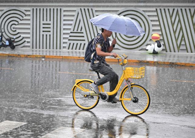A man rides a bicycle in the rain in Beijing on August 15, 2026. (Photo by ADEK BERRY / AFP)