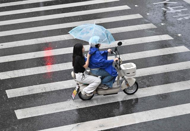 People ride a scooter in the rain in Beijing on August 15, 2026. (Photo by ADEK BERRY / AFP)