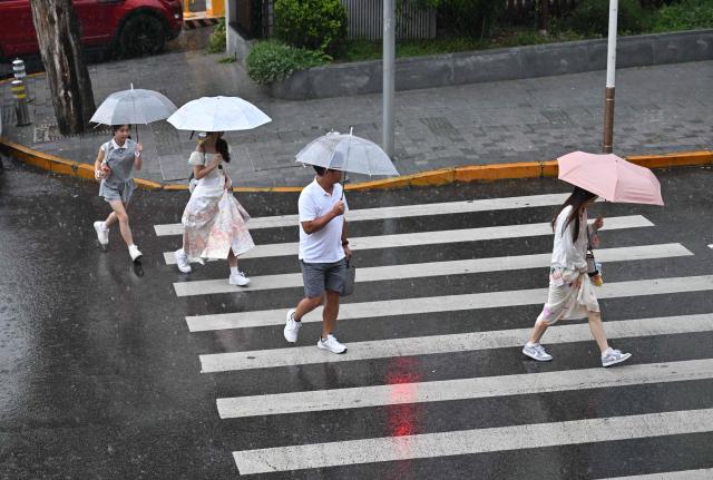 People cross a road in the rain in Beijing on August 15, 2026. (Photo by ADEK BERRY / AFP)