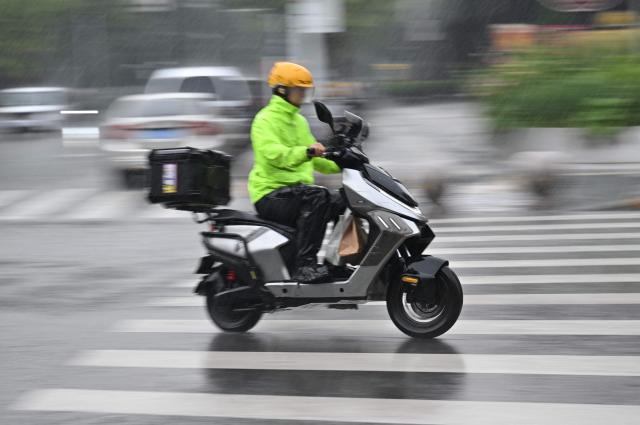 A man rides motorcycle in the rain in Beijing on August 15, 2026. (Photo by ADEK BERRY / AFP)