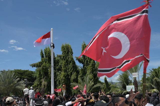 A man (top L) climbs a flagpole as he attempts to raise a Free Aceh Movement flag alongside the Indonesian national flag during a rally outside the Baiturrahman Grand Mosque in Banda Aceh, Aceh province, on August 15, 2026. Thousands of people gathered to mark the 21st anniversary of the Helsinki Memorandum of Understanding (MoU) peace agreement, which ended nearly three decades of conflict. The raising of the separatist-linked flag, although not explicitly banned by the 2005 peace deal, remains a highly controversial issue, with central government authorities often prohibiting its display. (Photo by Reza Saifullah / AFP)