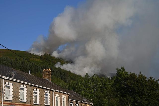 Smoke rises from burning moorland near a residential road, south of Ebbw Vale in south Wales on August 15, 2026. Around 200 military personnel have been deployed to a large area across South Wales to help battle wildfires. (Photo by JUSTIN TALLIS / AFP)