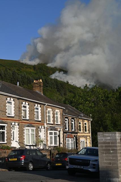 Smoke rises from burning moorland near a residential road, south of Ebbw Vale in south Wales on August 15, 2026. Around 200 military personnel have been deployed to a large area across South Wales to help battle wildfires. (Photo by JUSTIN TALLIS / AFP)