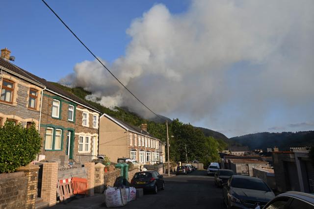 Smoke rises from burning moorland near a residential road, south of Ebbw Vale in south Wales on August 15, 2026. Around 200 military personnel have been deployed to a large area across South Wales to help battle wildfires. (Photo by JUSTIN TALLIS / AFP)