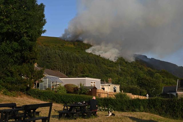 Smoke rises from burning moorland near a residential area, south of Ebbw Vale in south Wales on August 15, 2026. Around 200 military personnel have been deployed to a large area across South Wales to help battle wildfires. (Photo by JUSTIN TALLIS / AFP)