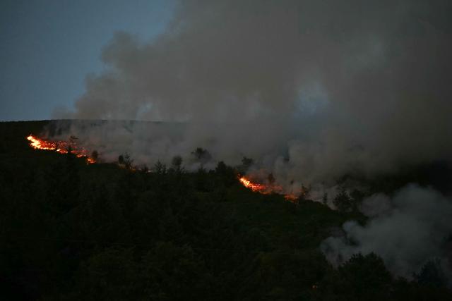 Smoke rises from burning moorland near a residential area, south of Ebbw Vale in south Wales on August 15, 2026. Around 200 military personnel have been deployed to a large area across South Wales to help battle wildfires. (Photo by JUSTIN TALLIS / AFP)