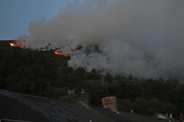 Smoke rises from burning moorland near a residential area, south of Ebbw Vale in south Wales on August 15, 2026. Around 200 military personnel have been deployed to a large area across South Wales to help battle wildfires. (Photo by JUSTIN TALLIS / AFP)