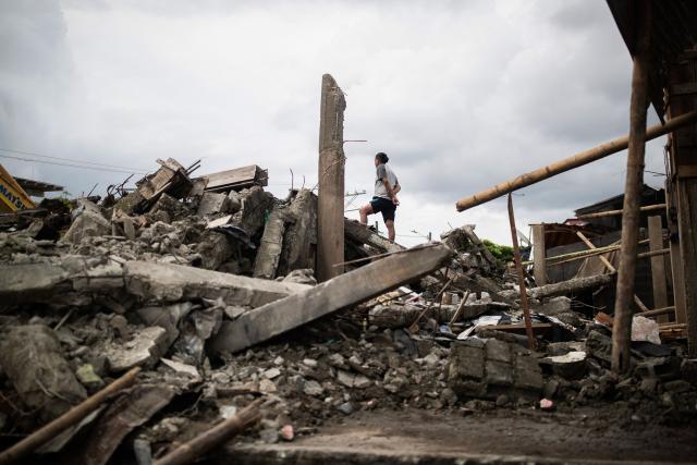 A man stands on top of some debris in the Medrano neighborhood of Quibdo, Choco department, Colombia, on August 15, 2026, days after a 7.4- magnitude earthquake. At least 287 people have died, thousands have been injured and about 379 remain unaccounted for, as the chances of finding earthquake survivors have dropped sharply since the critical 72-hour window passed, though volunteers and rescue crews continue digging through the rubble for any signs of life. (Photo by ESTEBAN VEGA LA-ROTTA / AFP)