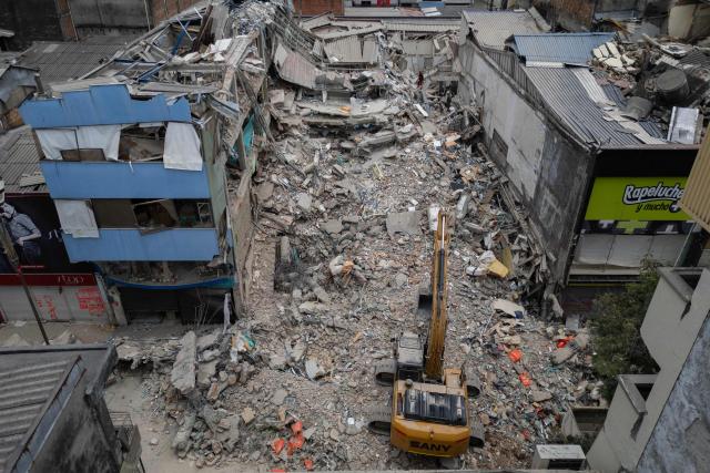 An aerial view shows a backhoe removing debris from collapsed buildings in Pereira, Colombia, on August 15, 2026, days after a 7.4 earthquake. At least 287 people have died, thousands have been injured and about 379 remain unaccounted for, while the chances of finding earthquake survivors have dropped sharply since the critical 72-hour window passed. (Photo by Luis ACOSTA / AFP)