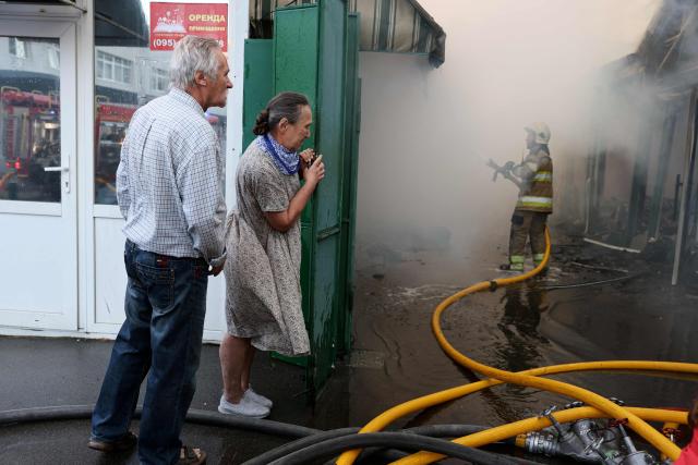 Local residents watch as a Ukrainian rescuer (R) works to extinguish a fire following a Russian strike in Kyiv on August 16, 2026, amid the Russian invasion of Ukraine. Russian strikes killed one person and wounded at least seven others in Ukraine, authorities said August 16, while Moscow officials reported downing more than 100 drones heading towards the capital. (Photo by AFP)