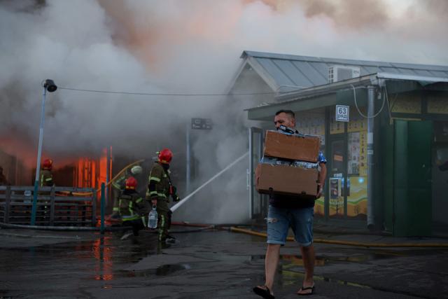 A man carries boxes of salvaged items from the burned-out book market as Ukrainian rescuers work to extinguish a fire following a Russian strike in Kyiv on August 16, 2026, amid the Russian invasion of Ukraine. Russian strikes killed one person and wounded at least seven others in Ukraine, authorities said August 16, while Moscow officials reported downing more than 100 drones heading towards the capital. (Photo by AFP)