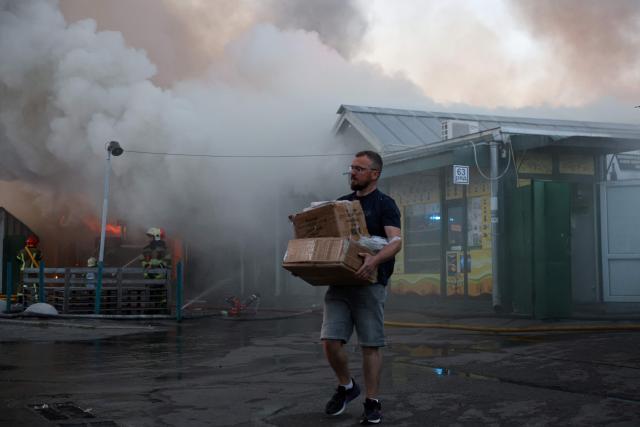 A man carries boxes of salvaged items from the burned-out book market as Ukrainian rescuers work to extinguish a fire following a Russian strike in Kyiv on August 16, 2026, amid the Russian invasion of Ukraine. Russian strikes killed one person and wounded at least seven others in Ukraine, authorities said August 16, while Moscow officials reported downing more than 100 drones heading towards the capital. (Photo by AFP)