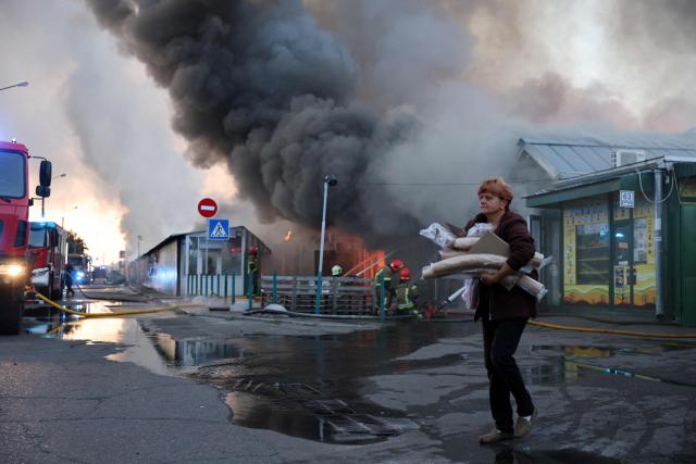 A woman carries salvaged items from the burned-out book market as Ukrainian rescuers work to extinguish a fire following a Russian strike in Kyiv on August 16, 2026, amid the Russian invasion of Ukraine. Russian strikes killed one person and wounded at least seven others in Ukraine, authorities said August 16, while Moscow officials reported downing more than 100 drones heading towards the capital. (Photo by AFP)