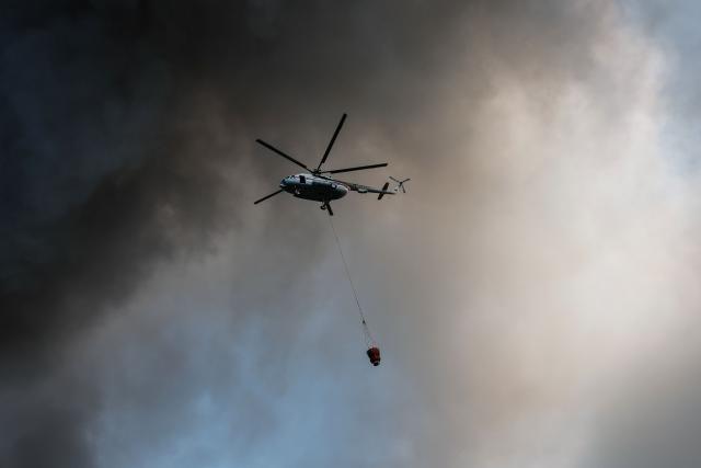 A firefighting helicopter attempts to extinguish a fire at the Russian e-commerce firm Wildberries' logistics complex near the town of Podolsk, outside Moscow on August 16, 2026. Hundreds of drones targeted Moscow on August 16, 2026 as Russia launched missile strikes that killed three people and wounded more than a dozen in Kyiv and other Ukrainian cities, officials on the two sides said. Ukraine has increasingly targeted warehouses linked to the Wildberries online retailer, arguing its strikes are a response to Moscow's bombardment of Ukrainian towns and infrastructure. (Photo by TATYANA MAKEYEVA / AFP)
