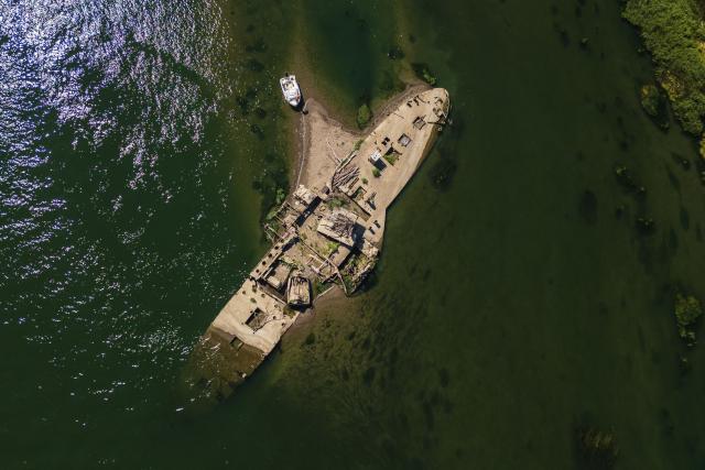 This aerial photograph shows the wreckage of the "Slovenac", a paddle-wheel tugboat built in 1913, emerging from the low waters of the Sava River near Sremska Mitrovica, Serbia, on August 16, 2026, as drought and prolonged hot and dry weather continue to lower water levels across the region. According to Serbian media and local historians, the Slovenac was a paddle-wheel steam tug powered by two steam engines. It sank on April 25, 1945, after striking a German mine while transporting supplies and wounded soldiers during the final days of World War II, and has since become a local landmark that reappears during periods of exceptionally low water. (Photo by Andrej ISAKOVIC / AFP)