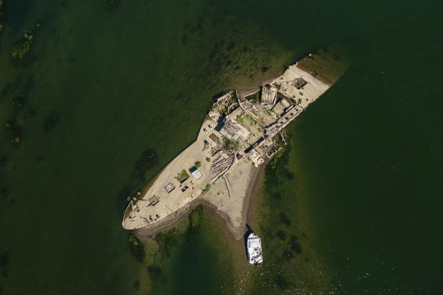 This aerial photograph shows the wreckage of the "Slovenac", a paddle-wheel tugboat built in 1913, emerging from the low waters of the Sava River near Sremska Mitrovica, Serbia, on August 16, 2026, as drought and prolonged hot and dry weather continue to lower water levels across the region. According to Serbian media and local historians, the Slovenac was a paddle-wheel steam tug powered by two steam engines. It sank on April 25, 1945, after striking a German mine while transporting supplies and wounded soldiers during the final days of World War II, and has since become a local landmark that reappears during periods of exceptionally low water. (Photo by Andrej ISAKOVIC / AFP)