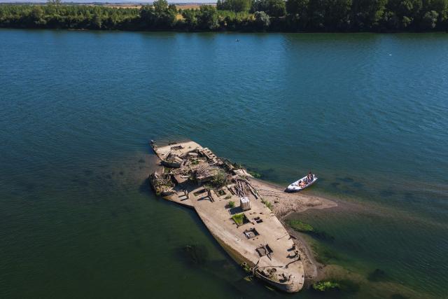 This aerial photograph shows the wreckage of the "Slovenac", a paddle-wheel tugboat built in 1913, emerging from the low waters of the Sava River near Sremska Mitrovica, Serbia, on August 16, 2026, as drought and prolonged hot and dry weather continue to lower water levels across the region. According to Serbian media and local historians, the Slovenac was a paddle-wheel steam tug powered by two steam engines. It sank on April 25, 1945, after striking a German mine while transporting supplies and wounded soldiers during the final days of World War II, and has since become a local landmark that reappears during periods of exceptionally low water. (Photo by Andrej ISAKOVIC / AFP)