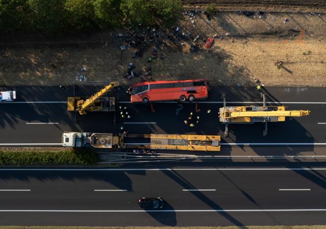 (ALTERNATIVE CROP) - This aerial view shows rescue workers and other officials working at the wreckage of an overturned Polish tourist bus on the M3 motorway near Mezokeresztes, about 150 km east of the Hungarian capital Budapest, on August 16, 2026. A Polish bus overturned on a Hungarian highway early Sunday, August 16, 2026, killing 12 people and leaving at least 10 with serious injuries, Hungary's Prime Minister Peter Magyar and officials said. The coach, heading from Serbia to Poland, crashed at 1:00 am (2300 GMT Saturday) on the M3 highway near Mezokeresztes, east of Budapest, according to a police statement. (Photo by Zoltan MATHE / MTI / AFP) / Hungary OUT