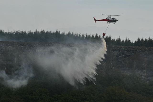 A helicopter drops water onto burning moorland south of Blaenavon in south Wales on August 16, 2026, as emergency services continue to battle wildfires thoughout the area. Around 200 military personnel have been deployed to a large area across South Wales to help battle wildfires. (Photo by JUSTIN TALLIS / AFP)