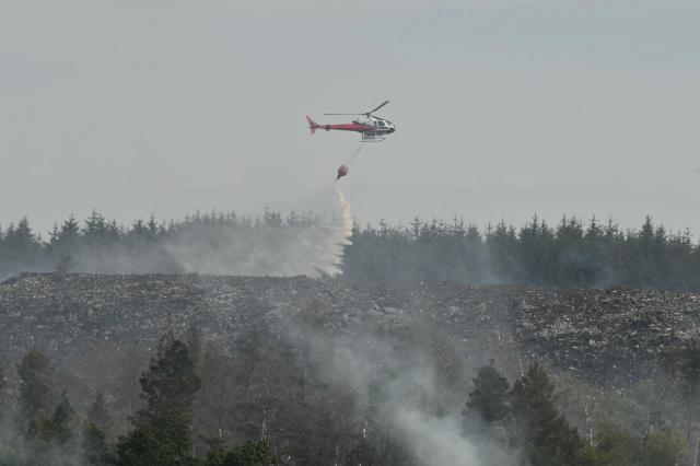 A helicopter drops water onto burning moorland south of Blaenavon in south Wales on August 16, 2026, as emergency services continue to battle wildfires thoughout the area. Around 200 military personnel have been deployed to a large area across South Wales to help battle wildfires. (Photo by JUSTIN TALLIS / AFP)