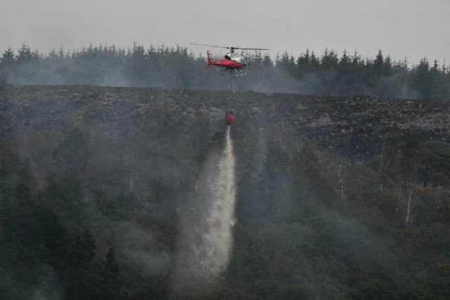A helicopter drops water onto burning moorland south of Blaenavon in south Wales on August 16, 2026, as emergency services continue to battle wildfires thoughout the area. Around 200 military personnel have been deployed to a large area across South Wales to help battle wildfires. (Photo by JUSTIN TALLIS / AFP)