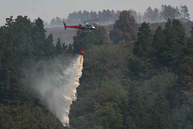 A helicopter drops water onto burning moorland south of Blaenavon in south Wales on August 16, 2026, as emergency services continue to battle wildfires thoughout the area. Around 200 military personnel have been deployed to a large area across South Wales to help battle wildfires. (Photo by JUSTIN TALLIS / AFP)