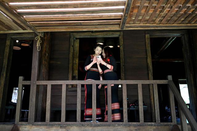 Women in traditional ethnic attire look at a mobile phone inside a stilt house in Dak Lak province on August 16, 2026. (Photo by Nhac NGUYEN / AFP)