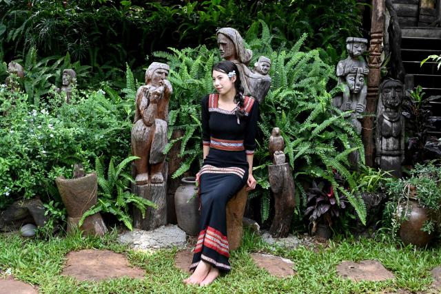 A woman in traditional ethnic attire poses for a photo with wooden statues in Dak Lak province on August 16, 2026. (Photo by Nhac NGUYEN / AFP)