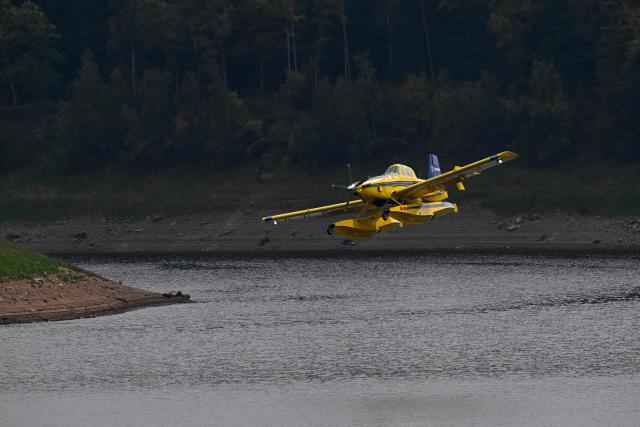 An SE-MHO Air Tractor AT-802A Fire Boss loads water from the Vesdre Dam, or Eupen Lake, during a wildfire burning in the Hautes Fagnes (High Fens) nature reserve, near Eupen, eastern Belgium on August 16, 2026. Hundreds of villagers were under evacuation orders in eastern Belgium on August 15, 2026 as firefighters battled one of the country's worst-ever wildfires, with vast swathes of nature reserve turned to a singed wasteland. Reinforcements were pulled from across the country to fight the blaze that broke out on August 14, 2026 in the High Fens park near the German border and quickly spread, with helicopters and water bombers flying in from across the EU to help. (Photo by JOHN THYS / AFP)