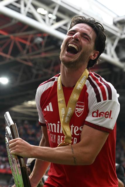Arsenal's English midfielder #41 Declan Rice laughs after being hit in the face by the strut back as he celebrates with the trophy on the pitch after their victory in the English FA Community Shield football match between Arsenal and Manchester City at The Principality Stadium, in Cardiff, south Wales on August 16, 2026. Arsenal won the game 3-0. (Photo by Glyn KIRK / AFP)