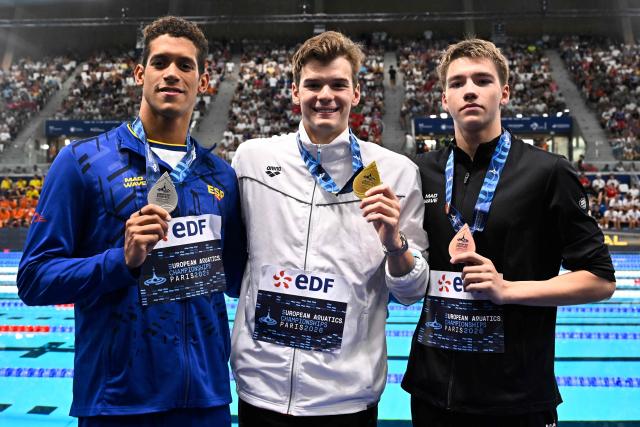 (LtoR) Spain's Hugo Gonzalez De Oliveira (silver medal), Hungary's Hubert Kos (gold medal) and Neutral athlete B Mikhail Shcherbakov (bronze medal) pose on the podium of the men's 200m individual medley swimming event during the LEN European Aquatics Championships at the Olympic Aquatic Centre in Saint-Denis, northern suburbs of Paris, on August 16, 2026. (Photo by JULIEN DE ROSA / AFP)