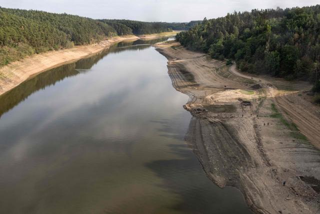 People wals on the bank of water reservoir Orlík - part of the Vltava Moldau river near Podolsko village on August 16, 2026 as water levels of the Vltava - Moldau river  have reached historic lows for almost last 65 years. (Photo by Michal Cizek / AFP)