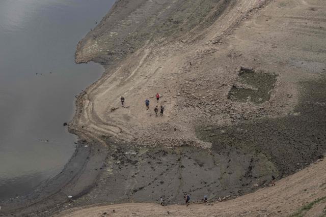 People walk on the bank of water reservoir Orlík - part of the Vltava Moldau river near Podolsko village on August 16, 2026 as water levels of the Vltava - Moldau river  have reached historic lows for almost last 65 years. (Photo by Michal Cizek / AFP)
