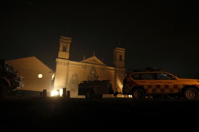 Firefighters of INFOAR Aragon forest fire prevention patrol in front of the San Juan de la Pena Monastery in Penas de Riglos, in the Spanish northeastern province of Aragon amid a wildfire that burnt 16,600 hectares on August 16, 2026. A Spanish soldier died on August 16, 2026 while helping efforts to extinguish a major wildfire in the northeastern region of Aragon that has raged for a week and threatened a 1,000-year-old monastery. Regional authorities said more than 16,600 hectares had been affected and around 1,000 people evacuated from various small settlements and villages. (Photo by Oscar DEL POZO / AFP)