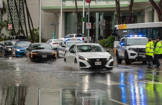 Vehicles make their way through a flooded intersection in front of the Hawaii Convention Center in Honolulu, Hawaii, on August 16, 2026. Hurricane Lala was pulling away from Hawaii's Big Island early Sunday, as heavy rain and strong winds struck the US Pacific state and officials warned of potentially dangerous flooding. The heavy rain and flood risk will then spread westward across the island chain on Sunday, according to the NHC. (Photo by Eugene Tanner / AFP)