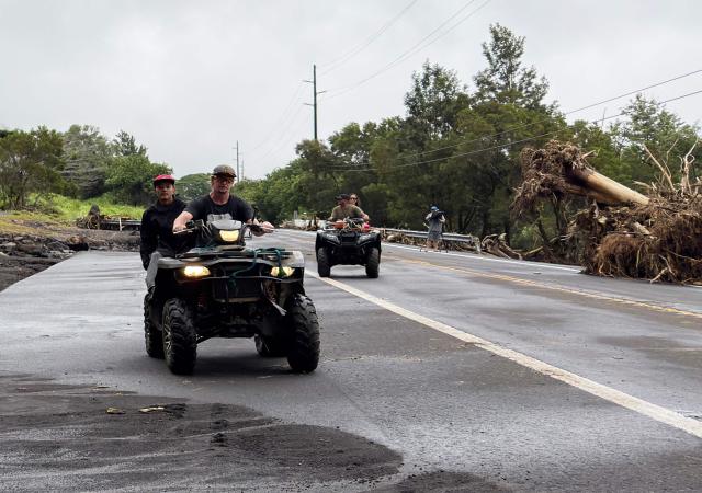 People ride on all terrain vehicles near uprooted trees near Pahala, on Hawaii Island on August 16, 2026. Hurricane Lala was pulling away from Hawaii's Big Island early Sunday, as heavy rain and strong winds struck the US Pacific state and officials warned of potentially dangerous flooding. The heavy rain and flood risk will then spread westward across the island chain on Sunday, according to the NHC. (Photo by Jill K. BRIGGS / AFP)