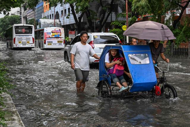 People commute through a flooded street due to the rains brought by the southwest monsoon in Manila on August 17, 2026. (Photo by Jam STA ROSA / AFP)
